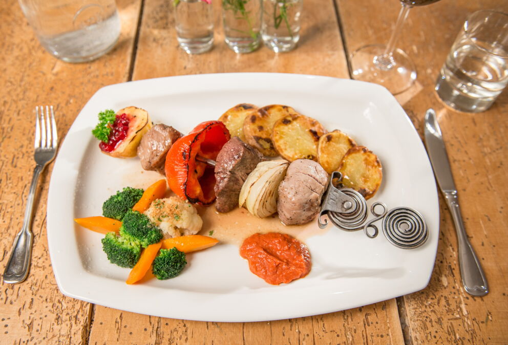 Fleischspieß mit gedämpftem Gemüse, gebackenen Kartoffeln und einer würzigen Soße im Restaurant Seewirt Zauner
