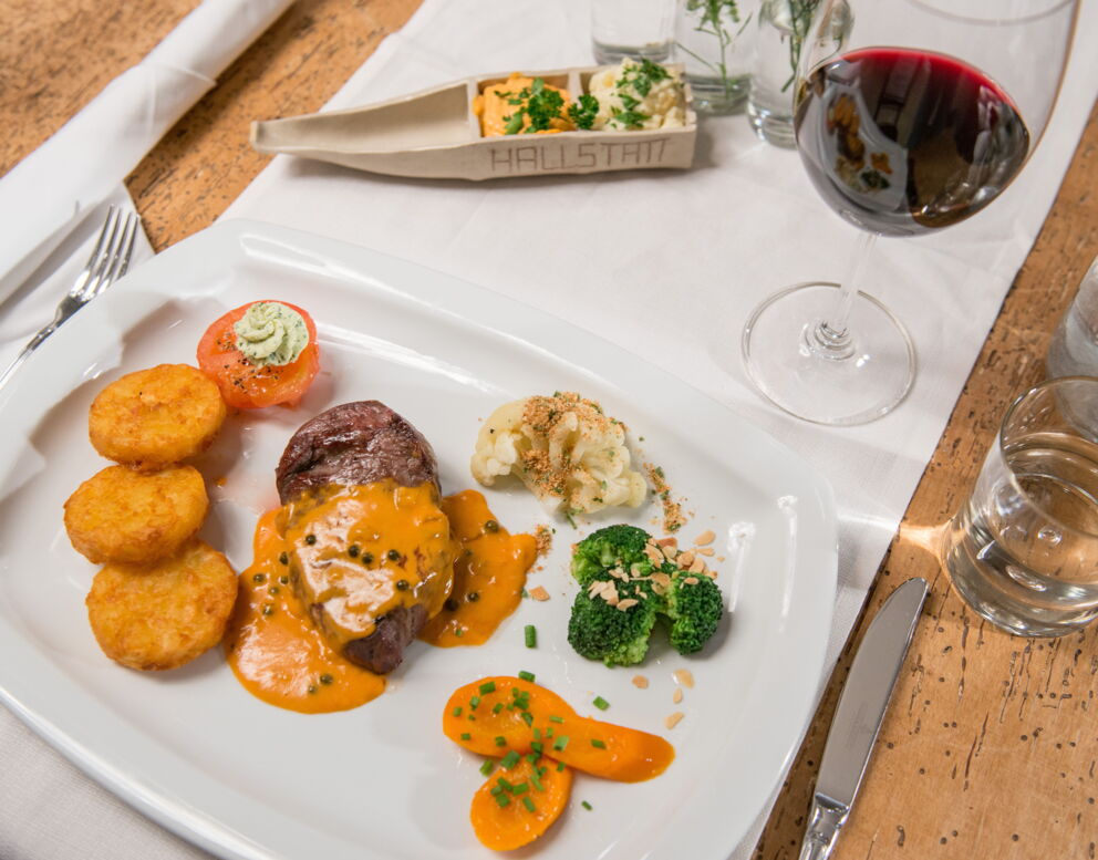 A steak with steamed vegetables, crispy potato slices and a delicious pepper sauce